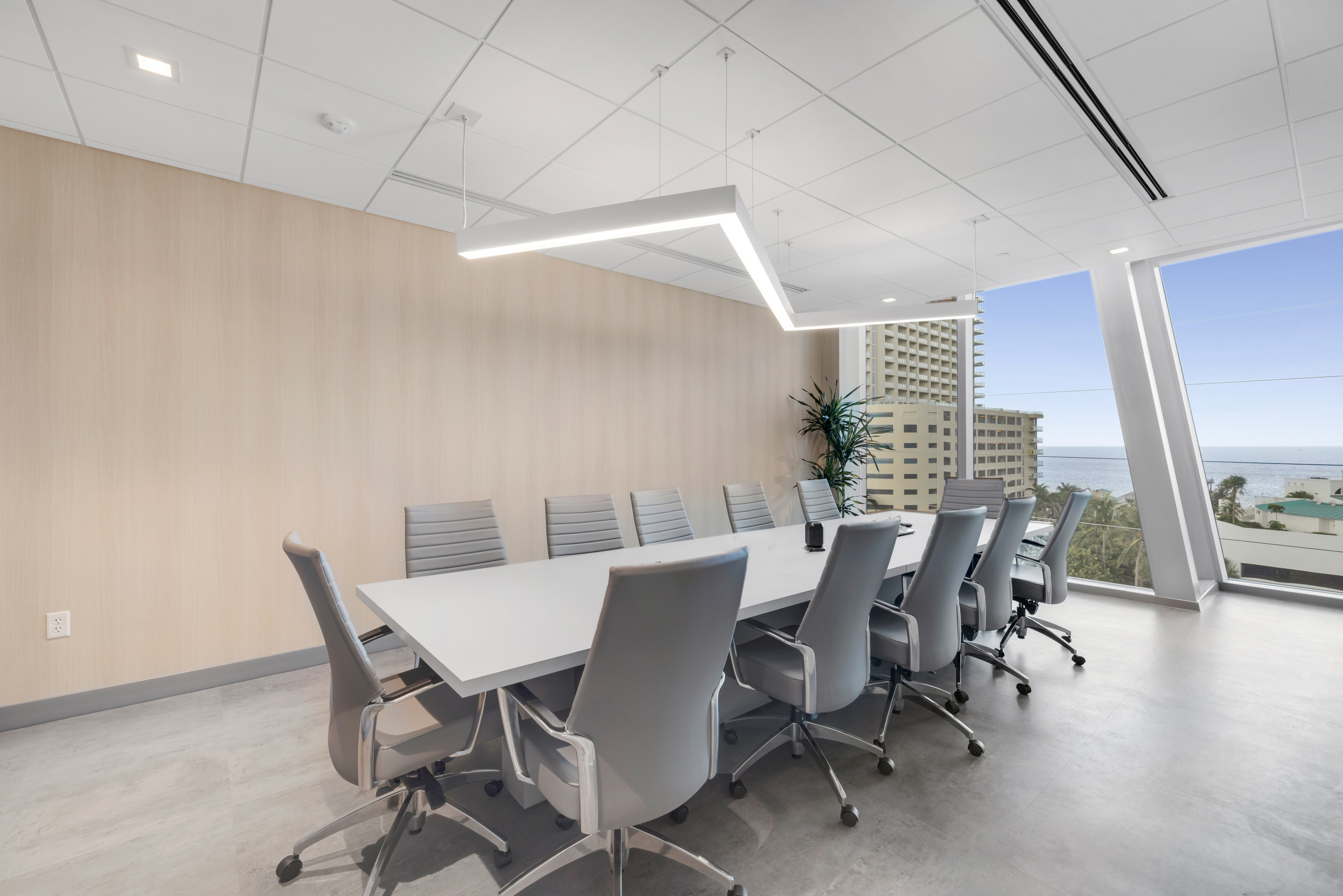 Professional boardroom office furniture: long wood veneer conference table and ergonomic tan leather swivel chairs in a bright, contemporary corporate meeting space.